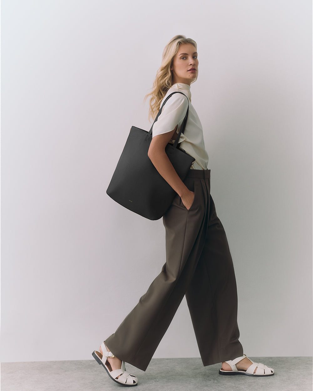Person wearing a white shirt, wide pants, sandals, and carrying a large shoulder bag.
