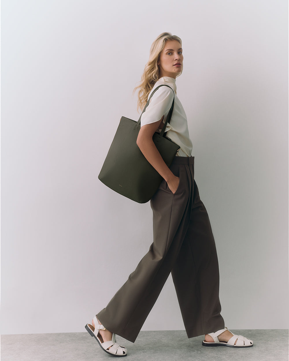 Person standing with a large tote bag wearing a t-shirt and wide-leg pants.