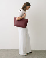 Person in white outfit carrying a large shoulder bag standing sideways.