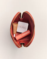 Open makeup bag with a tube of lip oil, a blush compact, and a cream eyeshadow inside.