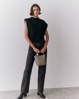 Person standing with small handbag wearing sleeveless top and jeans.