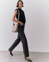 A person walking with a handbag, wearing a sleeveless top and pants.