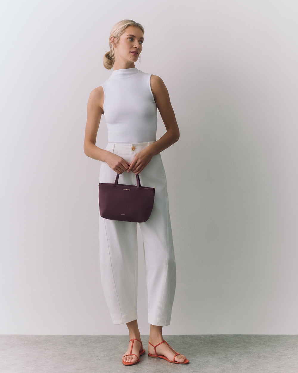 Person in sleeveless top and pants holding a small handbag, wearing sandals.