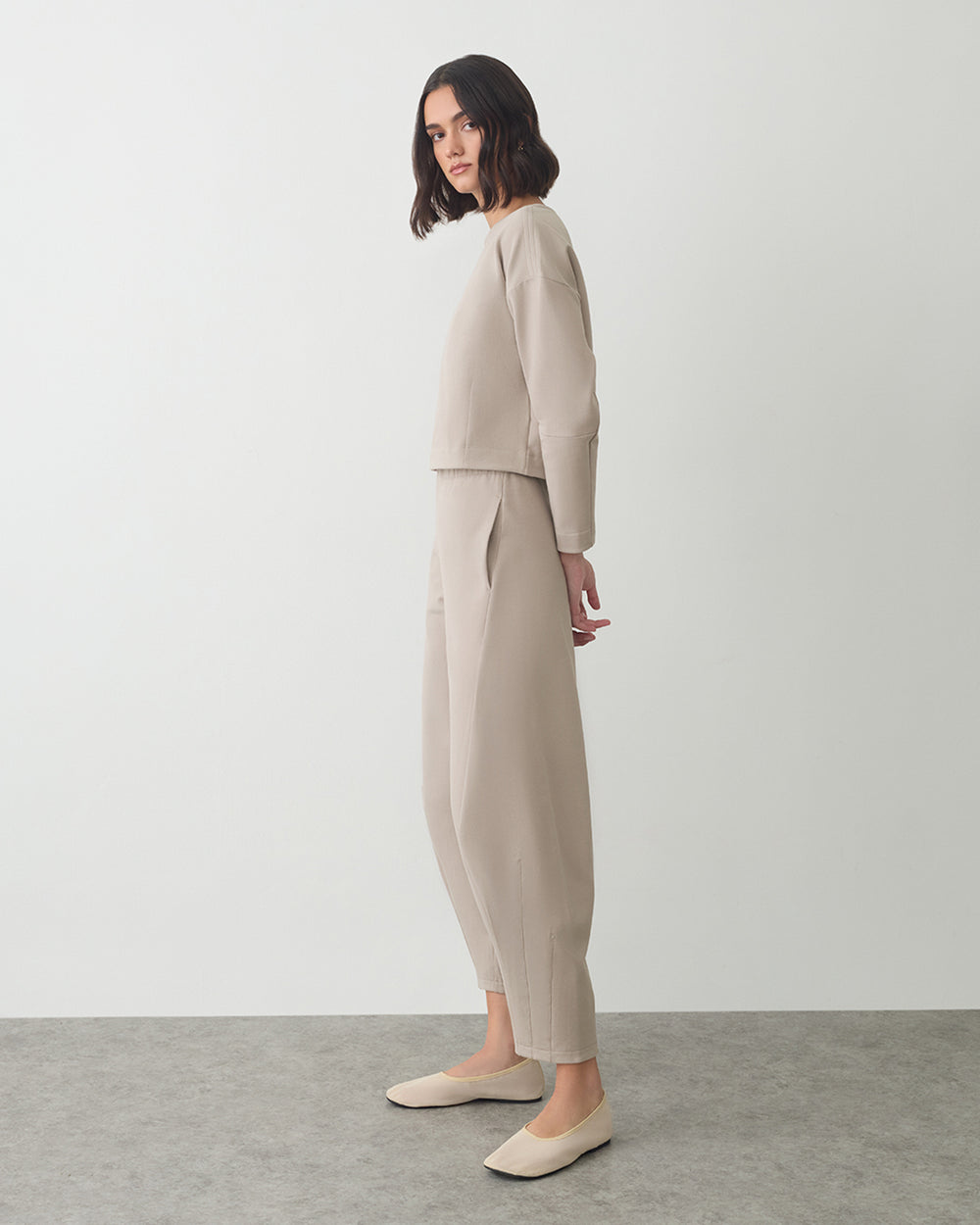 Person standing in a side pose wearing a matching top and pants with flats.