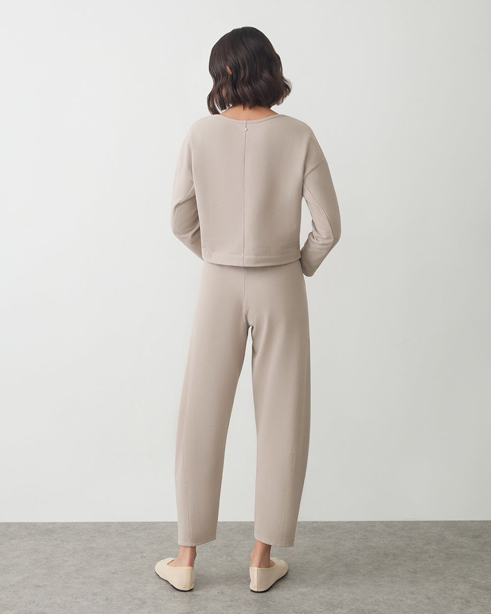 Person wearing a matching top and pants, standing with hands in pockets, facing away.