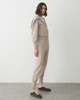 Person wearing a matching jacket and pants set with sneakers, standing sideways.