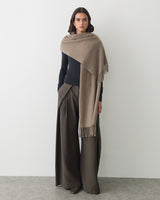Person wearing a cape, long-sleeve top, and wide-leg pants standing against a plain backdrop.