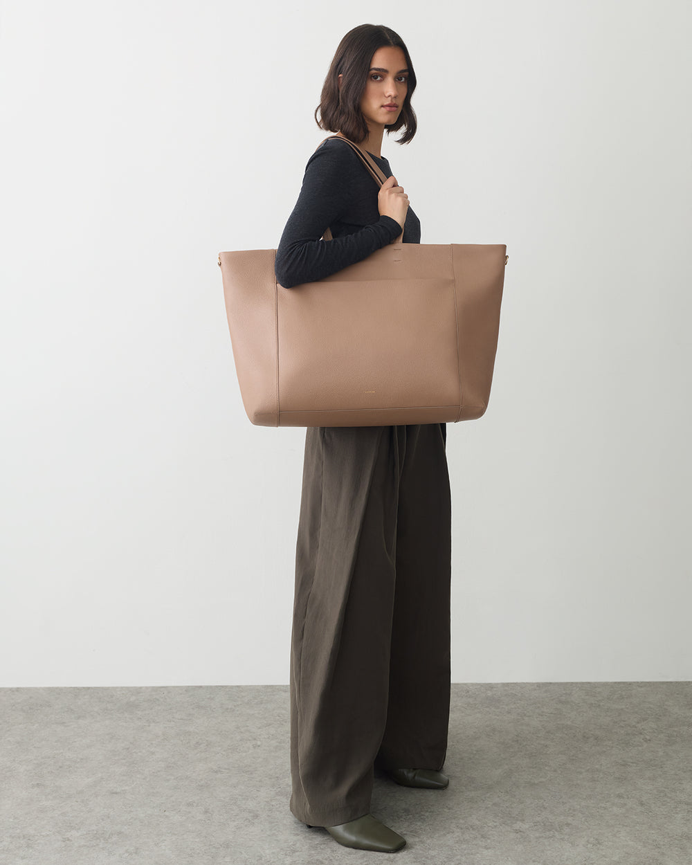 Person standing with a large tote bag over their shoulder, wearing long pants and a long-sleeve top.
