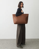 Person carrying a large tote bag, wearing wide-leg pants and a long-sleeve top.