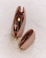 Two open makeup bags with brushes and cosmetics on a marble surface.