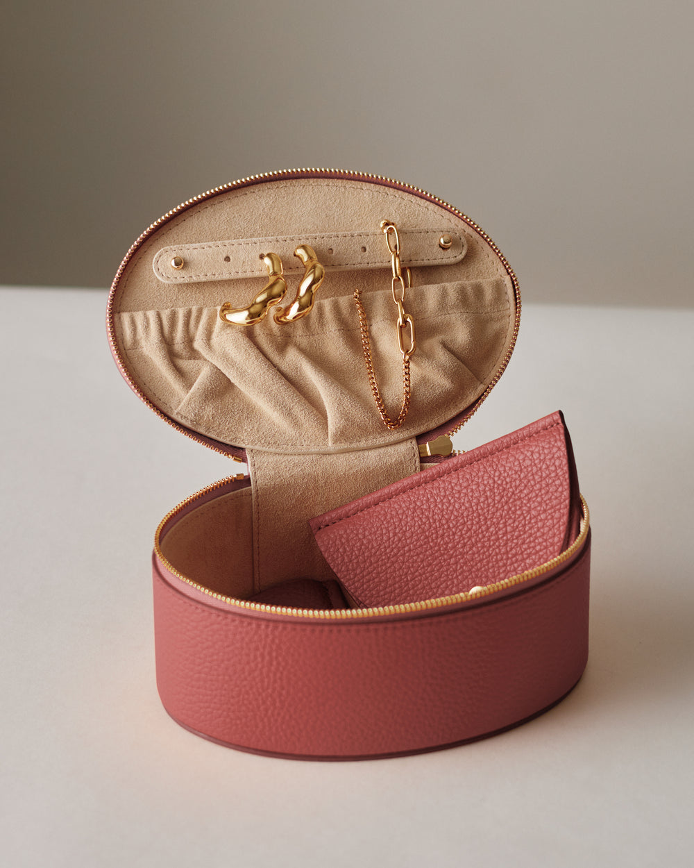 Open round jewelry case with earrings, bracelet, and small pouch inside.