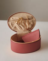 Open round jewelry case with earrings, bracelet, and small pouch inside.