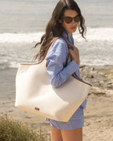 Person in striped outfit holding a tote bag near the beach.