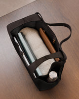 Open travel bag with a bottle, notebook, and fabric inside.