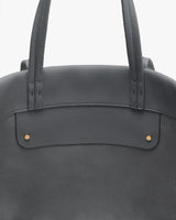 Close-up of a tote bag with two handles and gold stud details.
