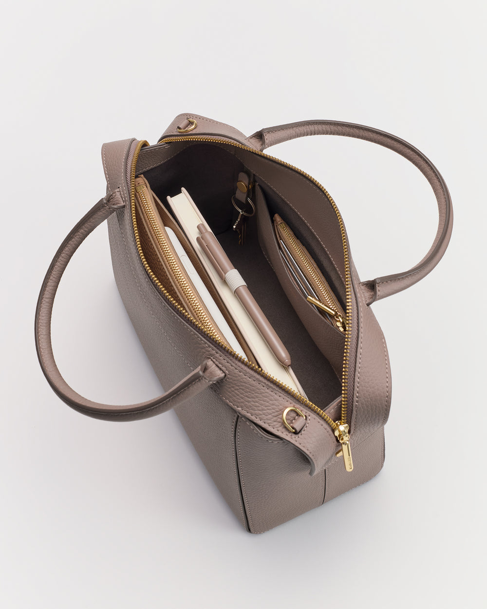 Open handbag with pen, notebook, and wallet inside, lying on a flat surface.