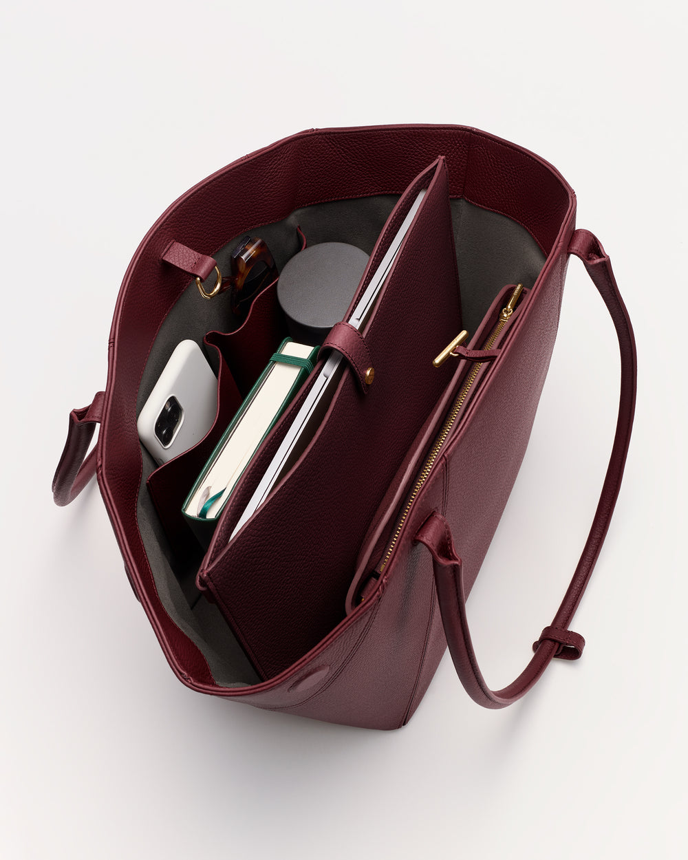 Open handbag with books, smartphone, and a small bottle inside.