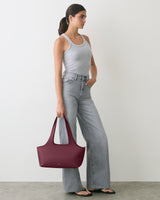 Person in tank top and jeans holding a handbag in a minimal setting.