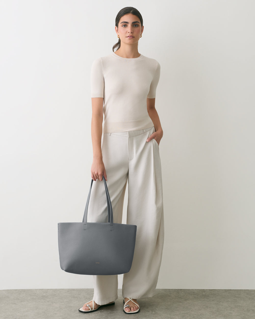Person wearing a short sleeve top and wide pants holds a large tote bag