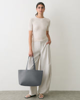 Person wearing a short sleeve top and wide pants holds a large tote bag