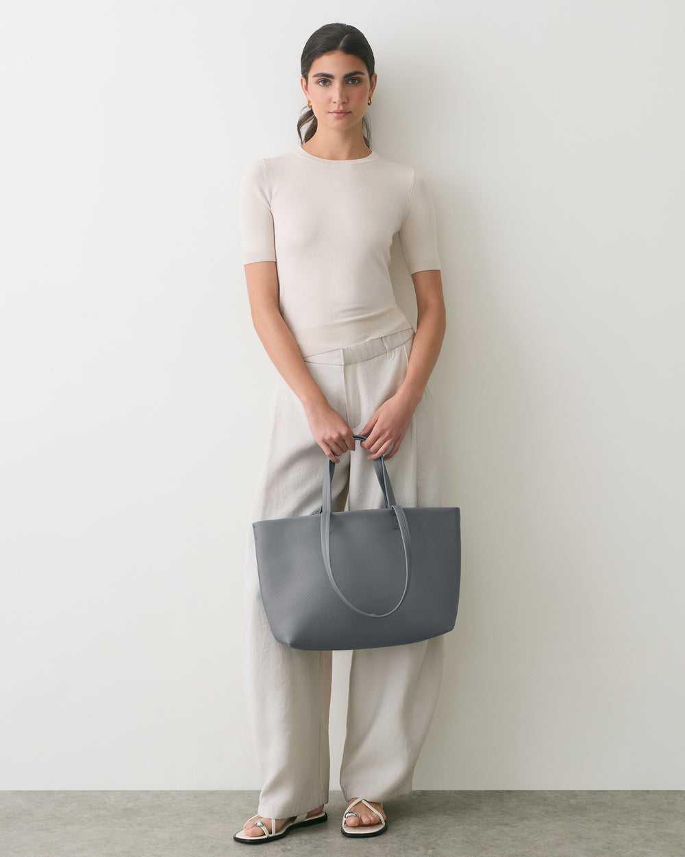 Person holding a large tote bag while wearing a short sleeve shirt and wide-leg pants