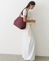 Person stands sideways with large handbag, wearing a long skirt and top.