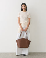 Person holding a large handbag, wearing a short-sleeved top and wide-leg pants.