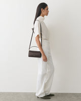Person in a turtleneck and pants with a shoulder bag, standing sideways.