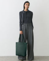 Person in long-sleeve top and wide pants holding a tote bag.