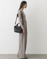 Woman in long-sleeve top and wide-leg pants carrying a shoulder bag.