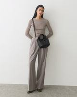 Person standing with a handbag, wearing a sweater and wide-leg pants.