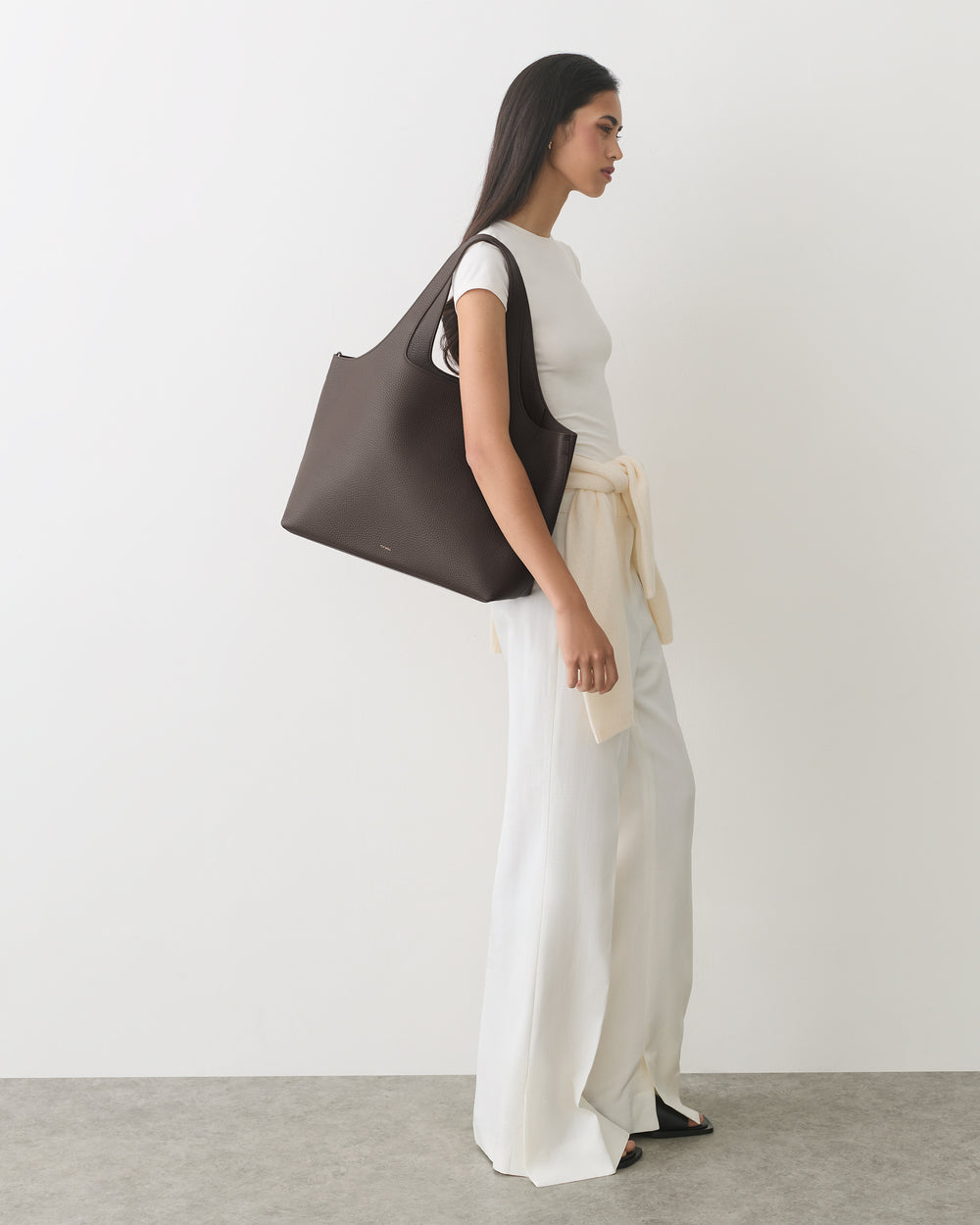 Person in sleeveless top and flowing pants carrying large shoulder bag.