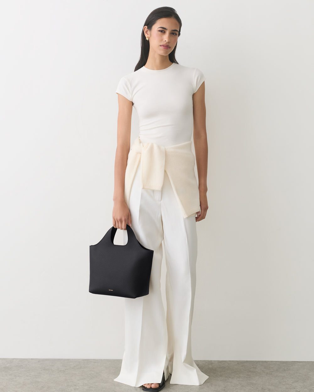 Person in a shirt and pants holding a handbag with a sweater around the waist