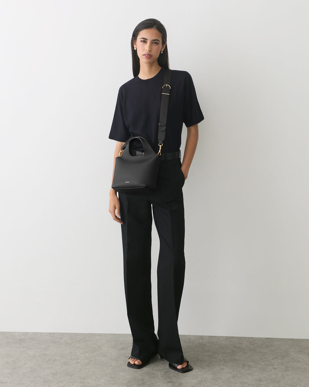 Person wearing a T-shirt and pants, holding a handbag with a shoulder strap.