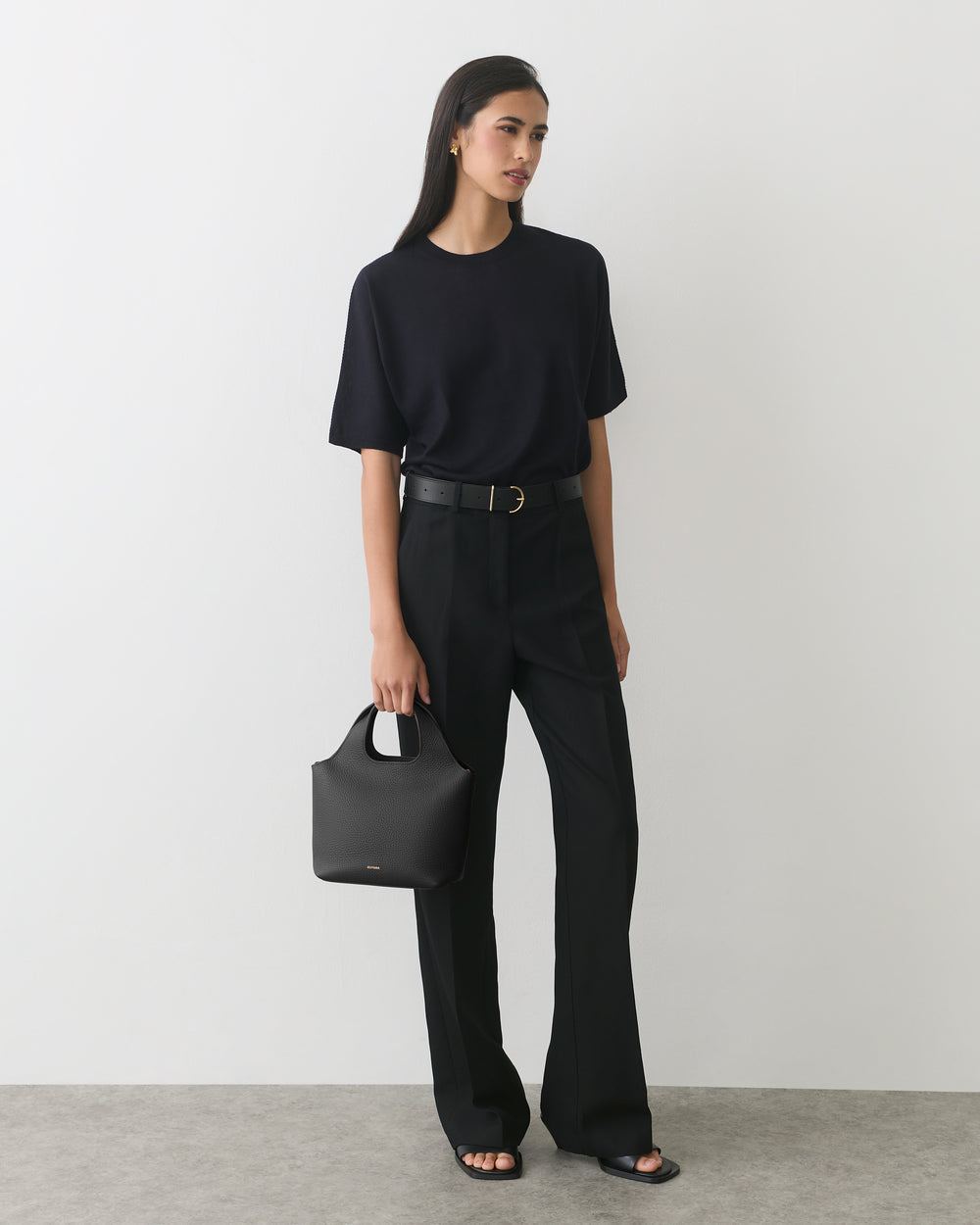 Person standing with a handbag wearing a t-shirt and trousers.