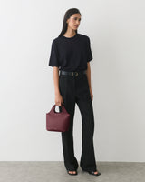 Person in a shirt and trousers holding a small handbag standing against a plain background.