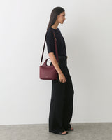 Person in fitted top and wide-legged pants with a shoulder bag, standing sideways.