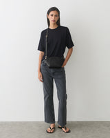 Person wearing t-shirt and jeans with a belt bag and sandals.