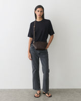 Person wearing a t-shirt, jeans, sandals, and a belt bag, standing against a plain background.