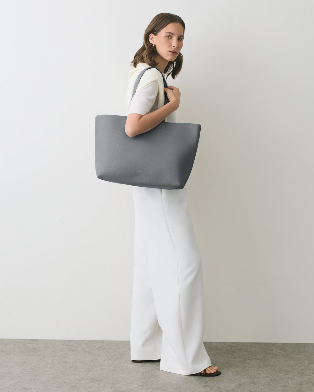 Person holding large handbag, standing against plain background wearing long pants.