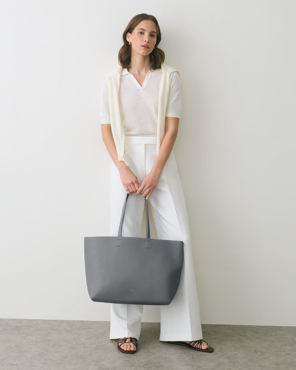 Person holding large tote bag, wearing casual outfit with sandals.