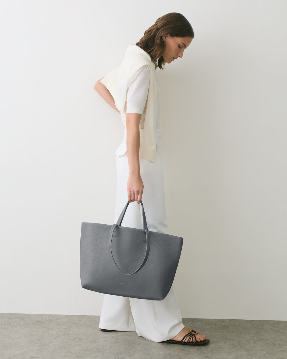 Person holding large handbag, wearing a sweater draped over shoulders.