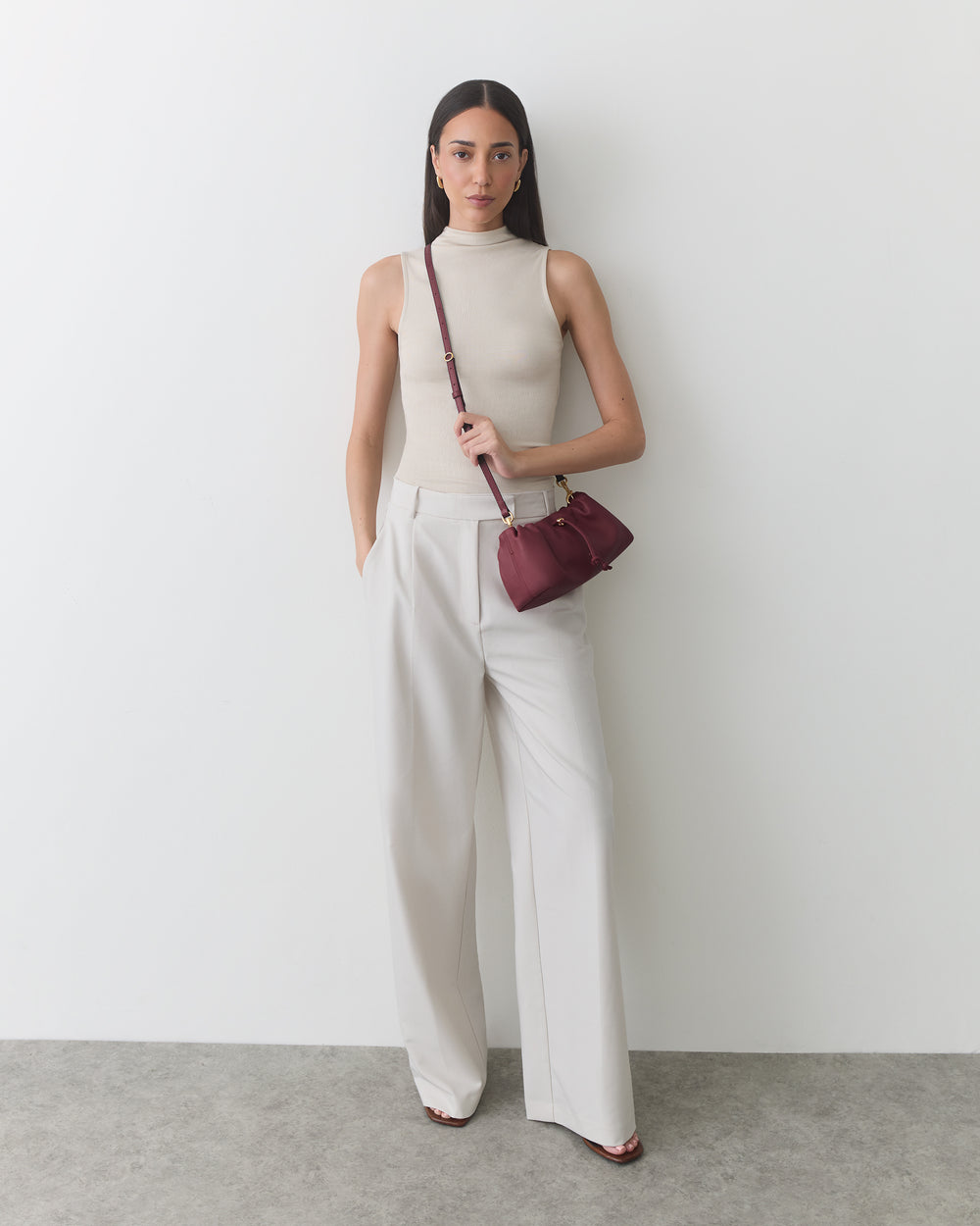 Person standing against a plain background holding a small crossbody bag.