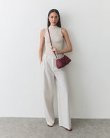 Person standing against a plain background holding a small crossbody bag.