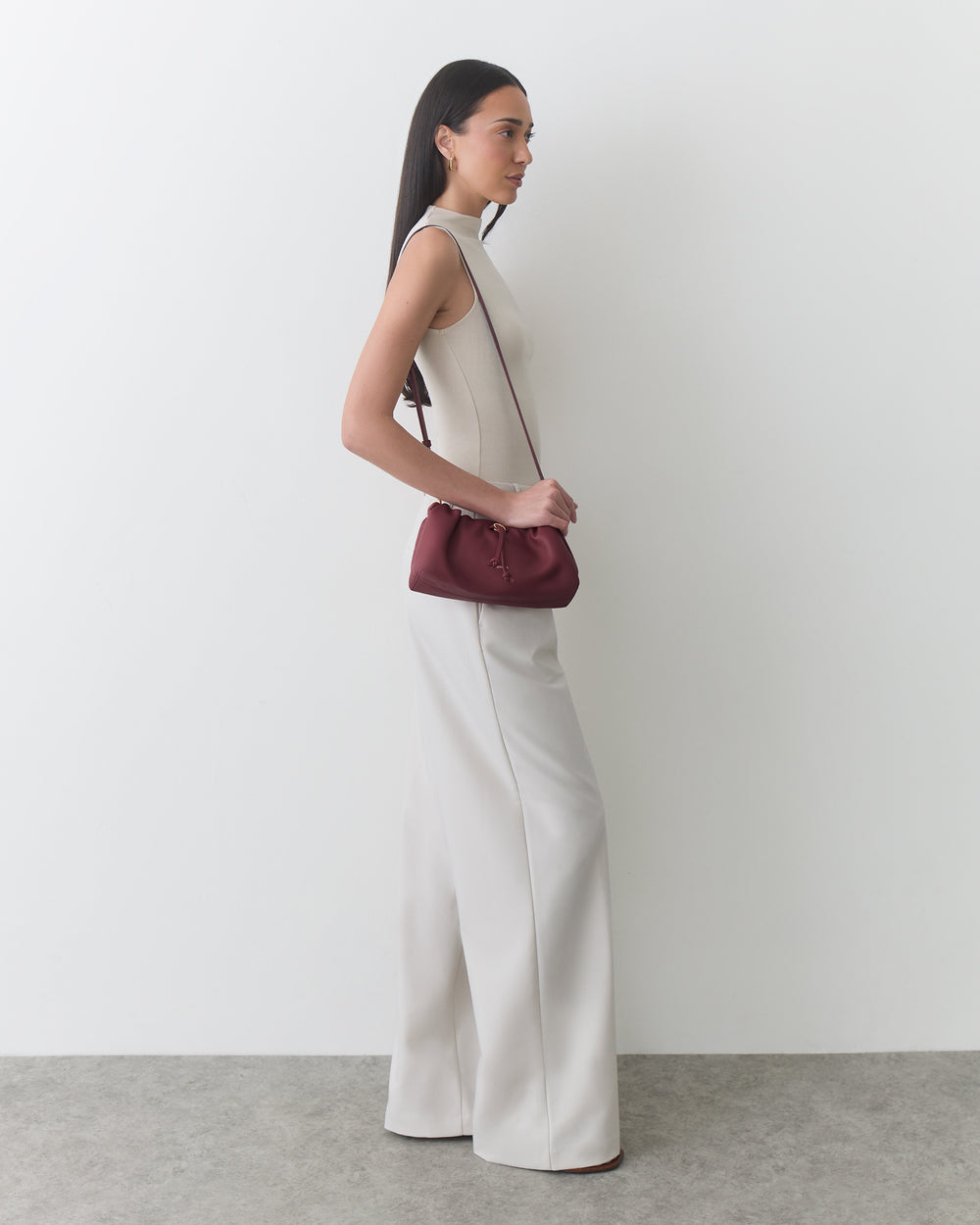 Person standing sideways with a small shoulder bag and wide-leg pants.