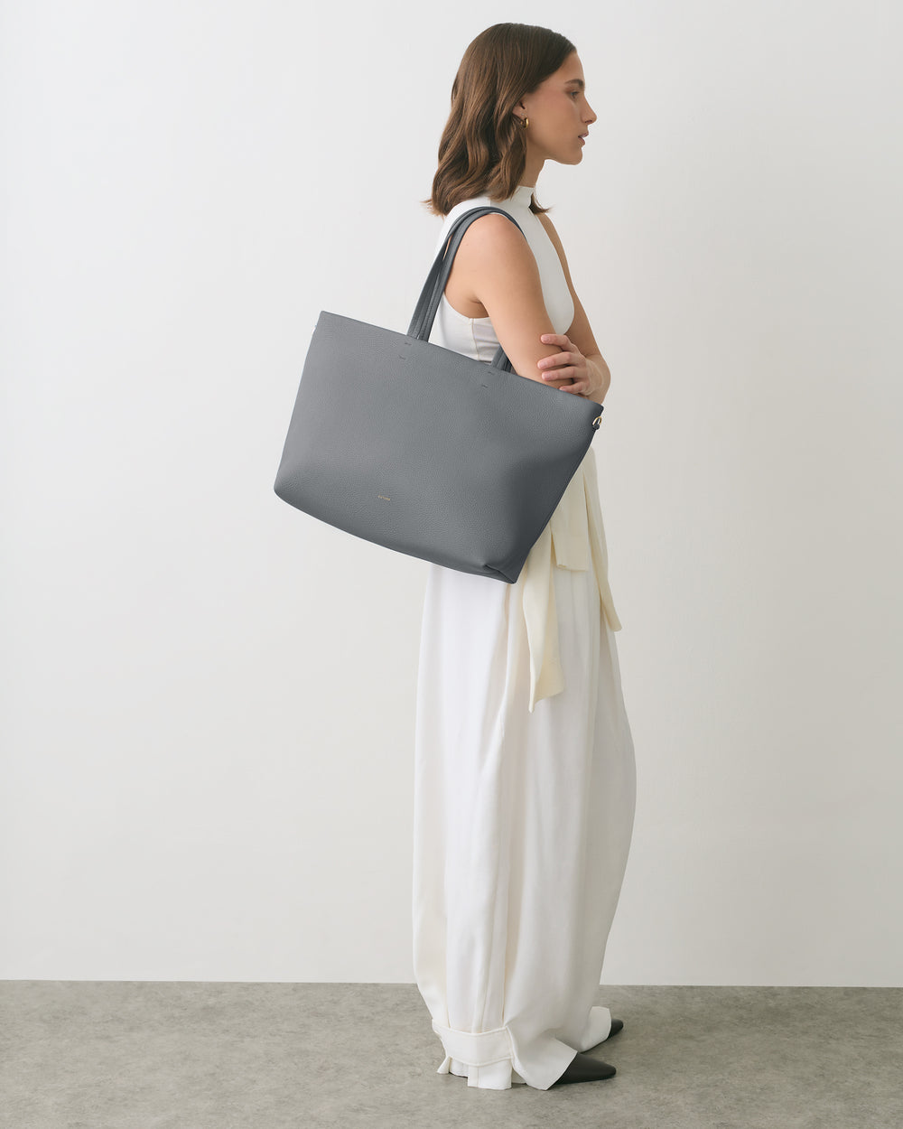 Person in white dress holding large tote bag, standing sideways.