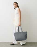 Person holding large tote bag, wearing sleeveless top and wide pants.