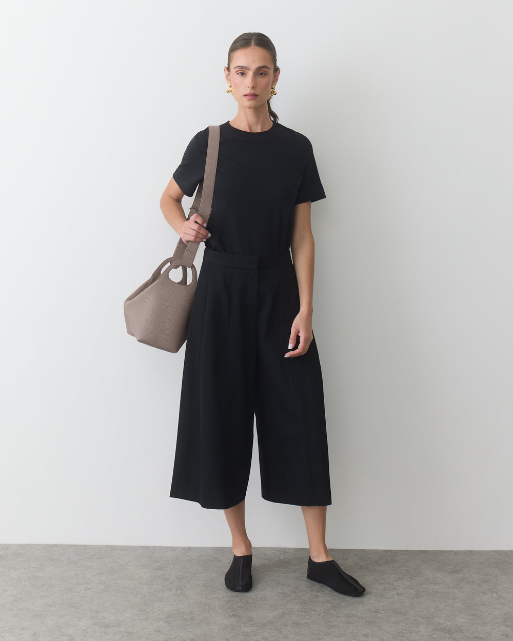 Person standing, holding a travel bag, wearing a T-shirt and wide-leg pants.