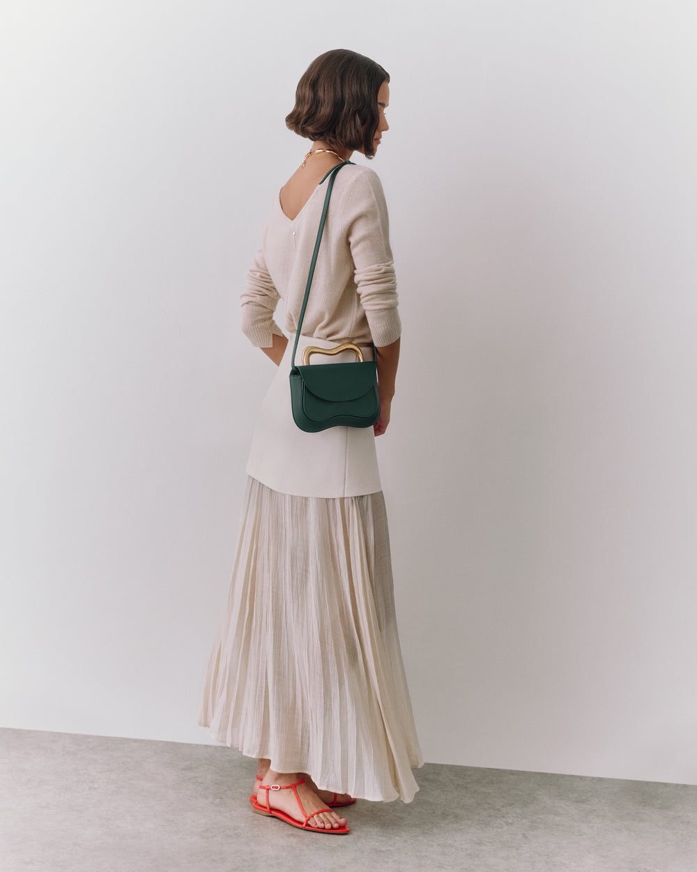 Person in long skirt and sweater with a small shoulder bag and sandals standing sideways