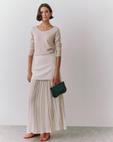 Person wearing a long skirt and top, holding a small purse.